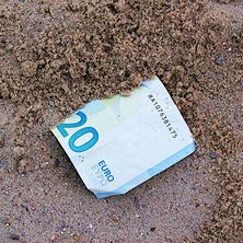 Foto eines halb von Sand bedeckten Geldscheins 